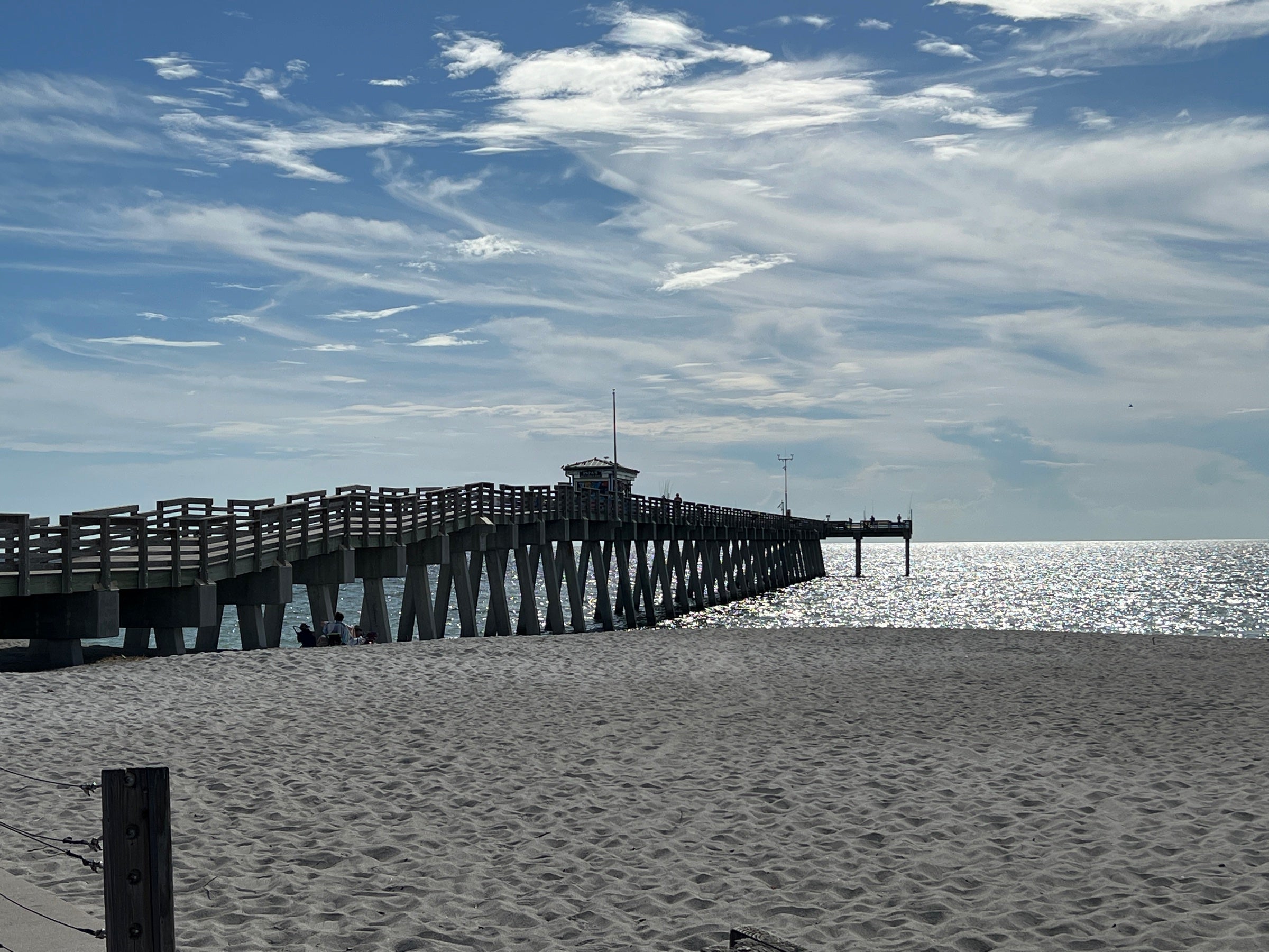 A wooden pier extending over the Pacific at a sandy California beach